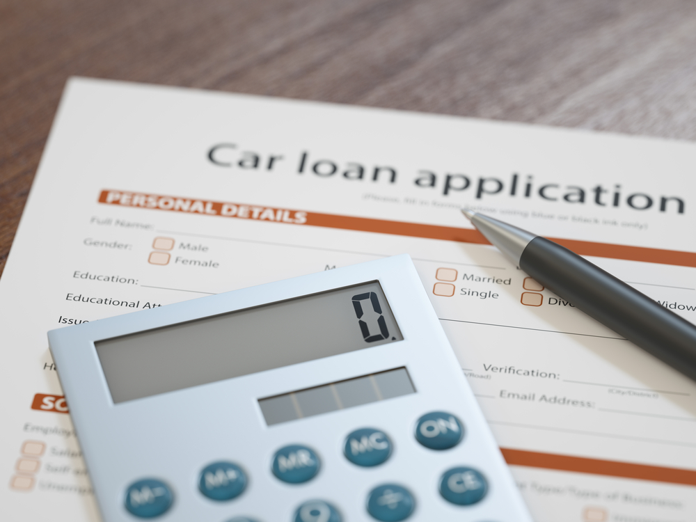Calculator on car loan application paperwork illustrating negative equity auto loan.