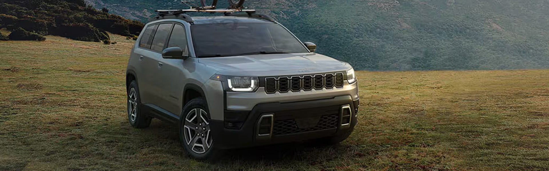 2027 Jeep Grand Cherokee: More Power, More Choice, and Proper Off-Road Hardware standing in a green land surrounded by mountains.